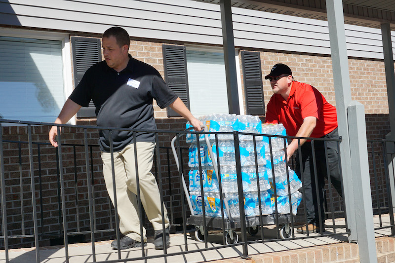 Two men transporting a trolly of bottled water 