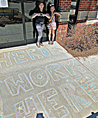 Adelyn and Malia's sidewalk chalk art reads "Heroes work here." 